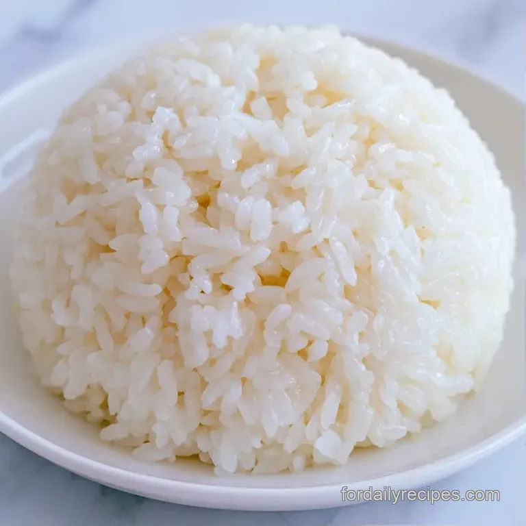 Neatly shaped white glutinous rice on a dark ceramic plate, accented by a small wooden spoon and a sprig of green.